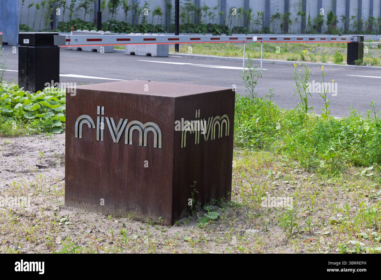 Insegna RIVM presso la loro sede centrale, con un cubo metallico intemprato con il logo, sullo sfondo di una strada ad accesso controllato e di una vegetazione lussureggiante. Foto Stock