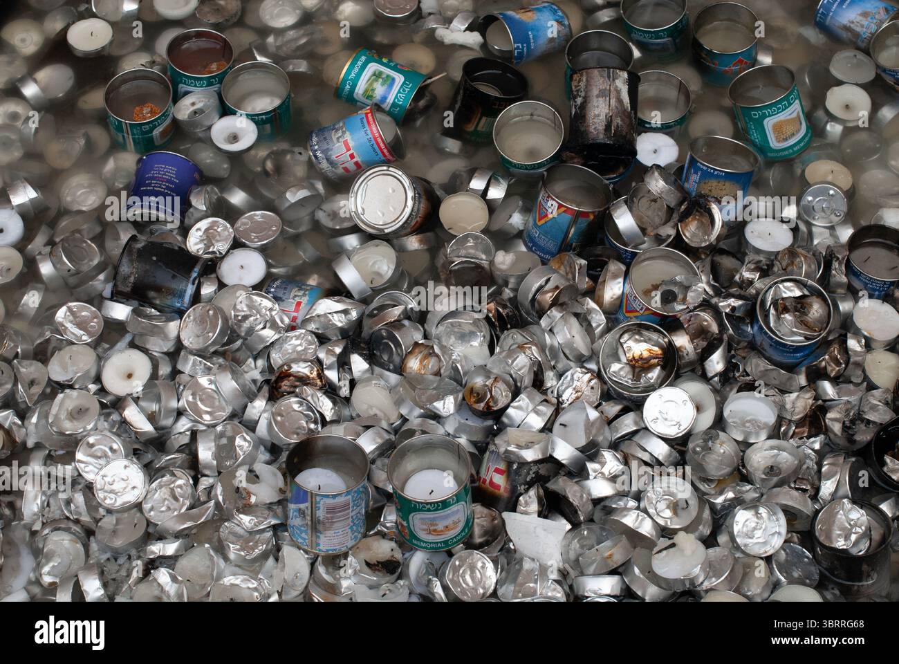 I contenitori di candele blu e di metallo e le candele di tè bruciate come memoriale per i morti dell'Ebraismo vengono gettati fuori da una tomba in Israele. Foto Stock