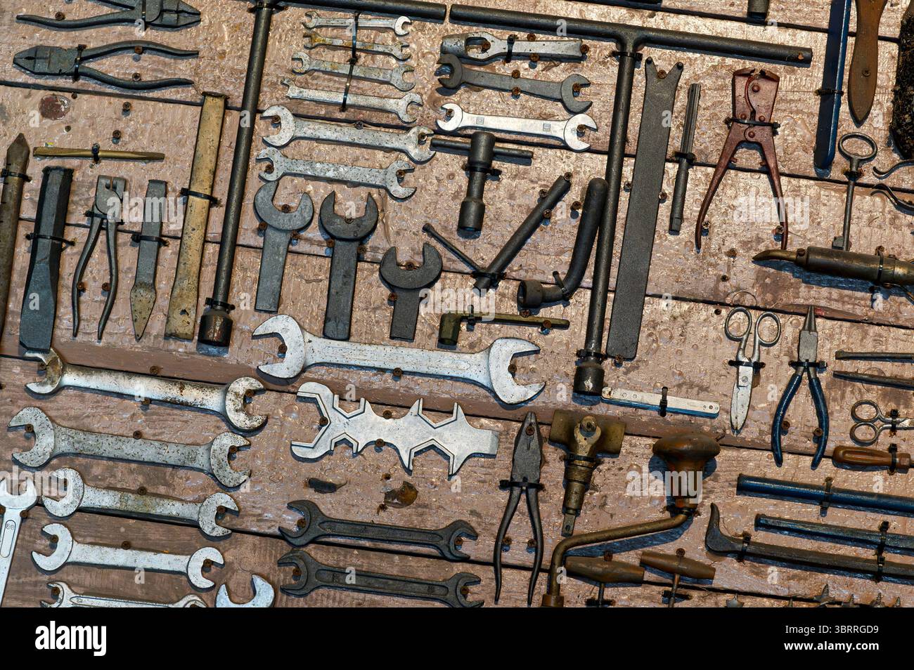 Vari vecchi strumenti appesi su un asse di legno, creando uno sfondo vintage e rustico perfetto per l'artigianato e i concetti di riparazione Foto Stock