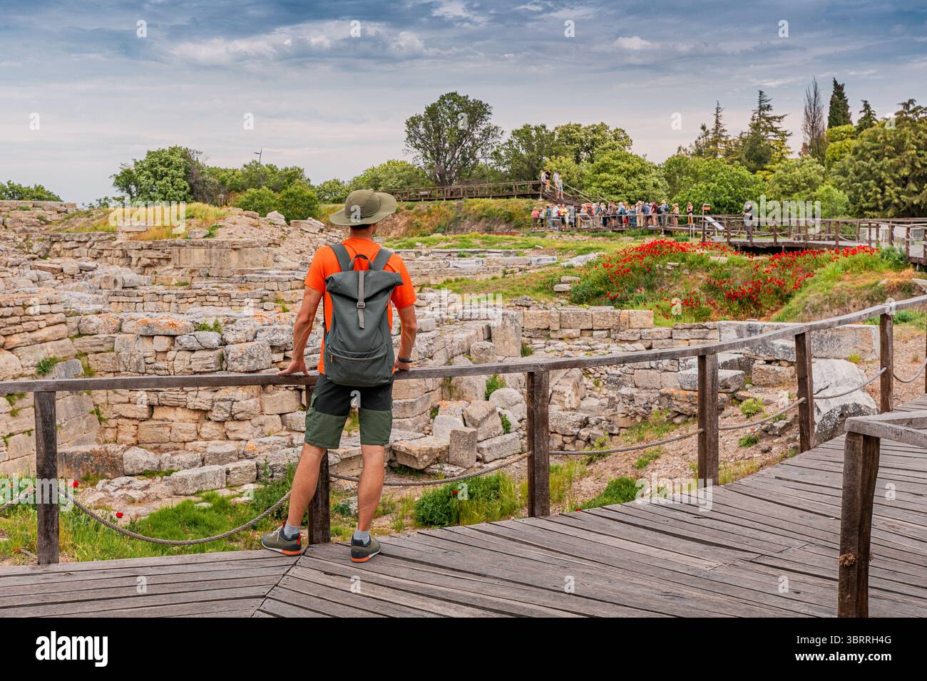 Turista che indossa una maglietta arancione e uno zaino che guarda le rovine di Troia, un sito archeologico in Turchia Foto Stock