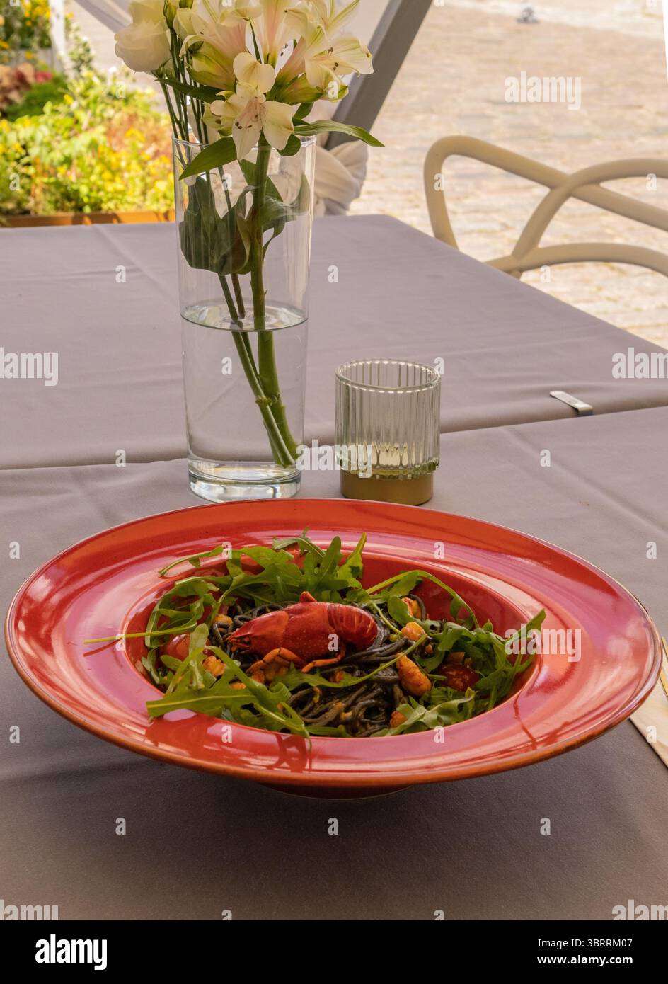Un'elegante insalata di pesce che combina verdure fresche e crostacei, decorata ad arte su un vivace piatto rosso allestito su un tavolo da pranzo all'aperto con ligh naturale Foto Stock