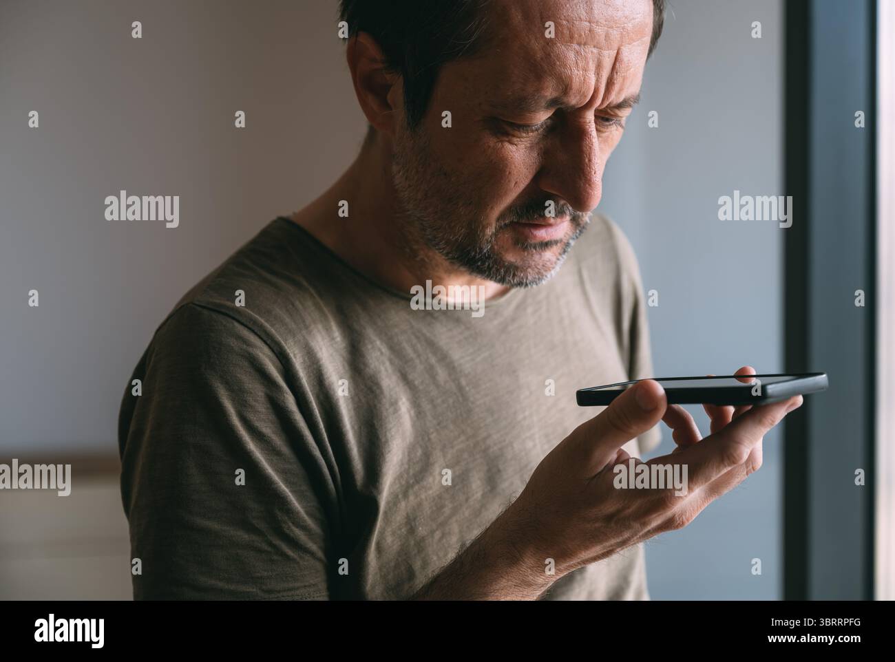 Tenendo il telefono davanti al viso e parlando, un uomo che parla al telefono cellulare tenendo il dispositivo lontano dalla bocca, messa a fuoco selettiva Foto Stock