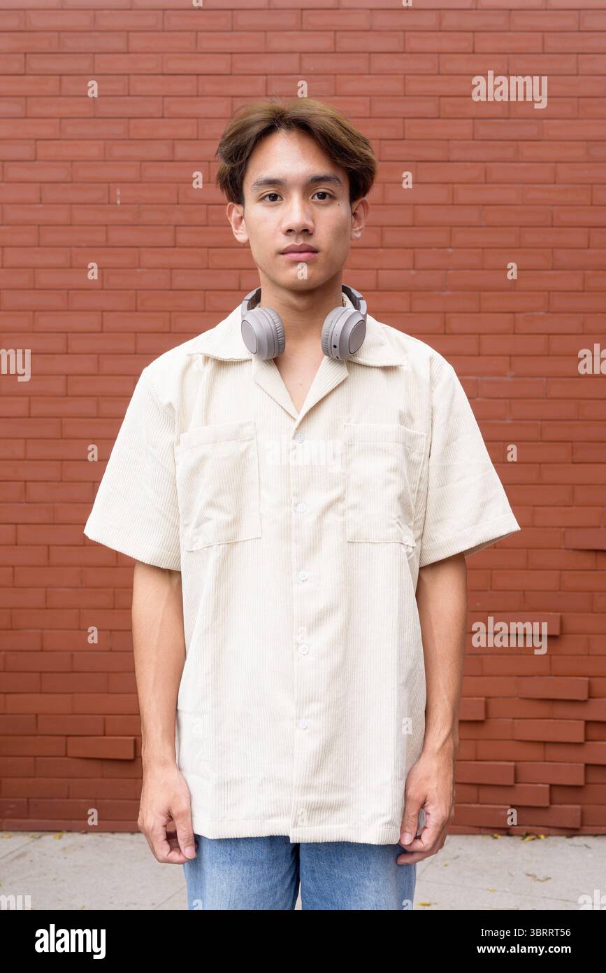 Ritratto di non binario carino asiatico giovane gay uomo contro muro di mattoni Foto Stock