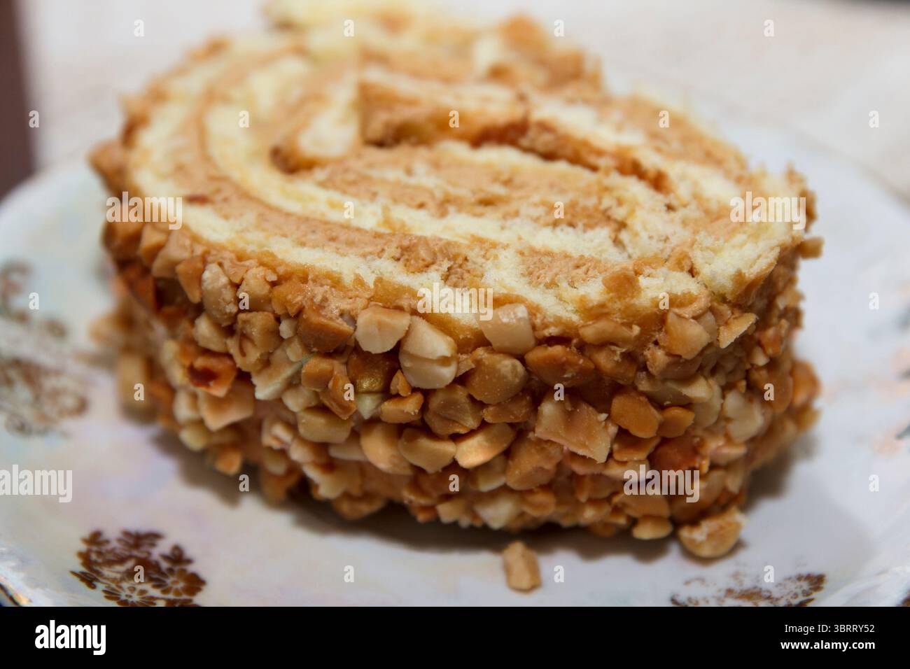 Fetta di pan di Spagna arrotolata con strati di panna e noci tritate, fotografata su un piatto decorativo, concetto di dessert fatto in casa Foto Stock