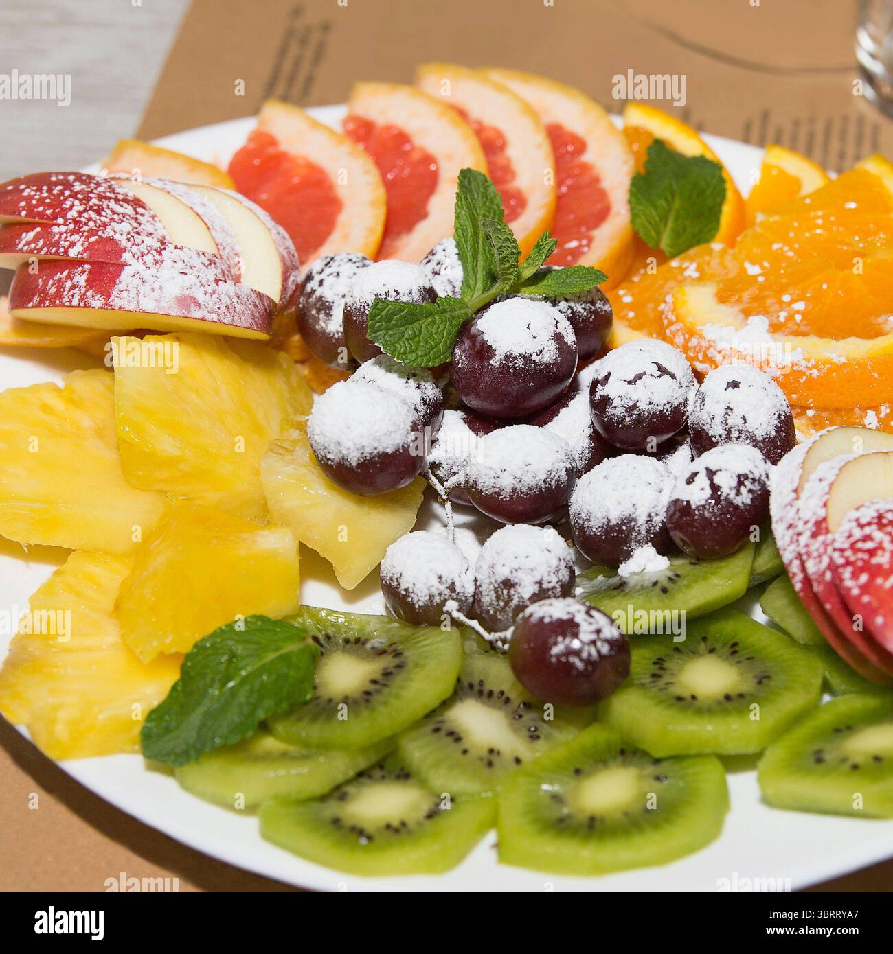 Piatto colorato di frutta a fette come kiwi, uva, arance, mele e ananas con zucchero a velo, servito su un tavolo per una sana alimentazione Foto Stock