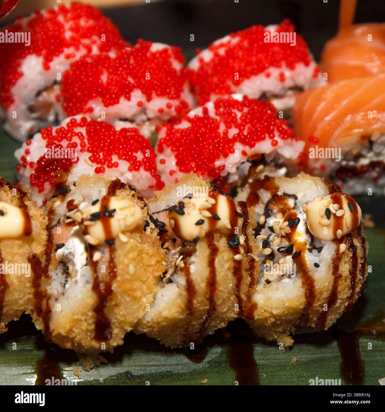 Primo piano di sushi roll assortiti con tempura croccante, tobiko e salmone fresco, catturati con luce naturale su uno sfondo scuro Foto Stock