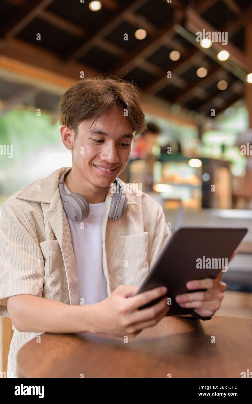 Bel giovane uomo asiatico non binario che siede in un bar ristorante Foto Stock