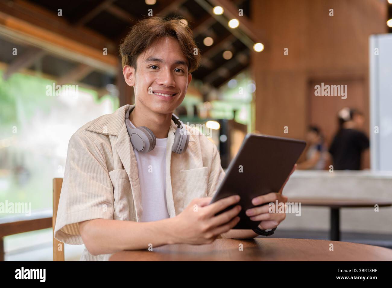 Bel giovane uomo asiatico non binario che siede in un bar ristorante Foto Stock