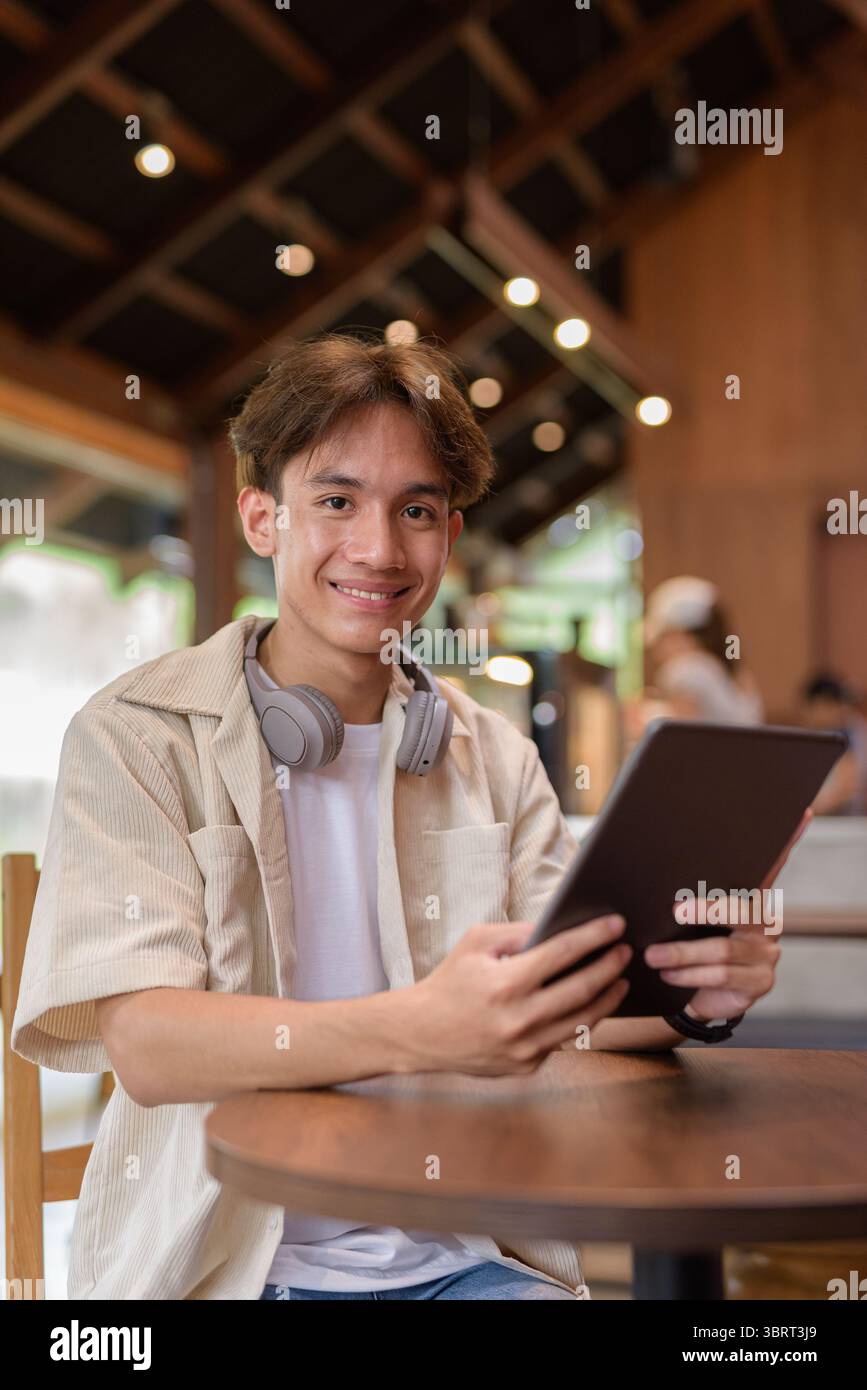 Bel giovane uomo asiatico non binario che siede in un bar ristorante Foto Stock