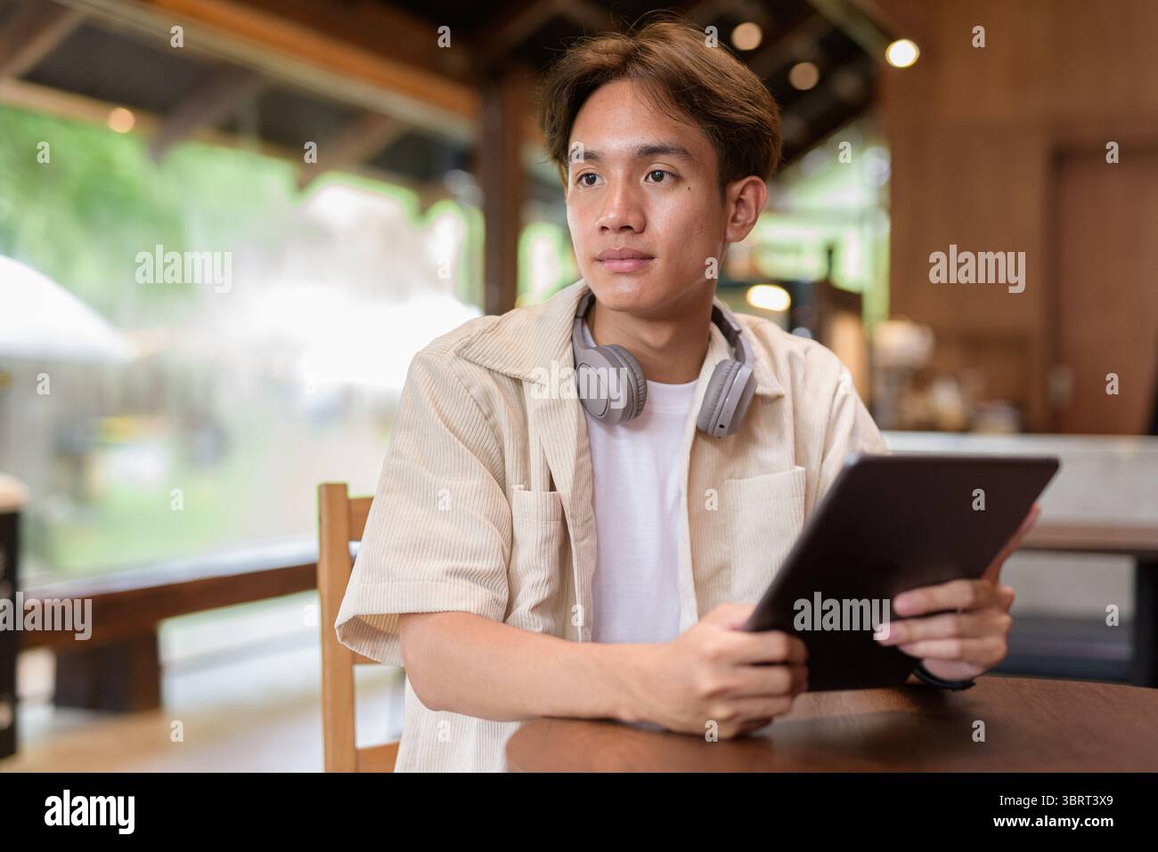 Bel giovane uomo asiatico non binario che siede in un bar ristorante Foto Stock