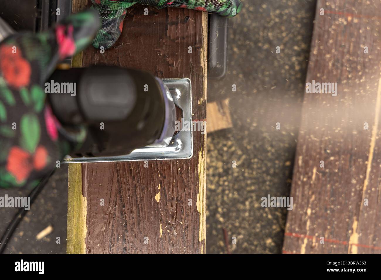 Una donna che indossa guanti protettivi colorati taglia le tavole in giardino utilizzando un seghetto elettrico. Taglieri per un ponte giardino, costruzione di una veranda, o Foto Stock