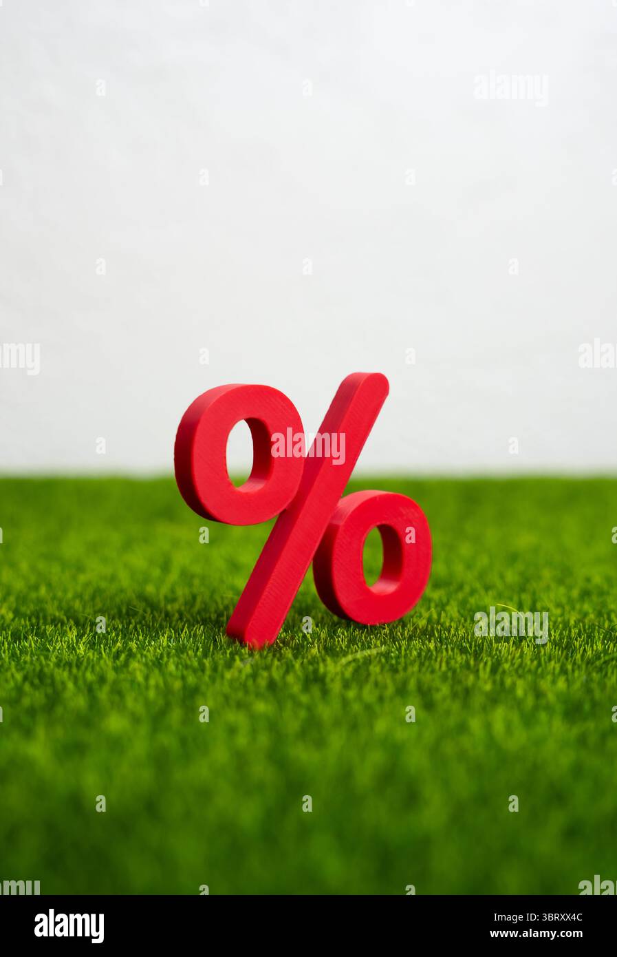 Percentuale rossa sull'erba verde. Concetto di maturità e pronto a raccogliere profitti sul deposito del tasso di interesse. Crescita del risparmio, o finanziaria favorevole Foto Stock