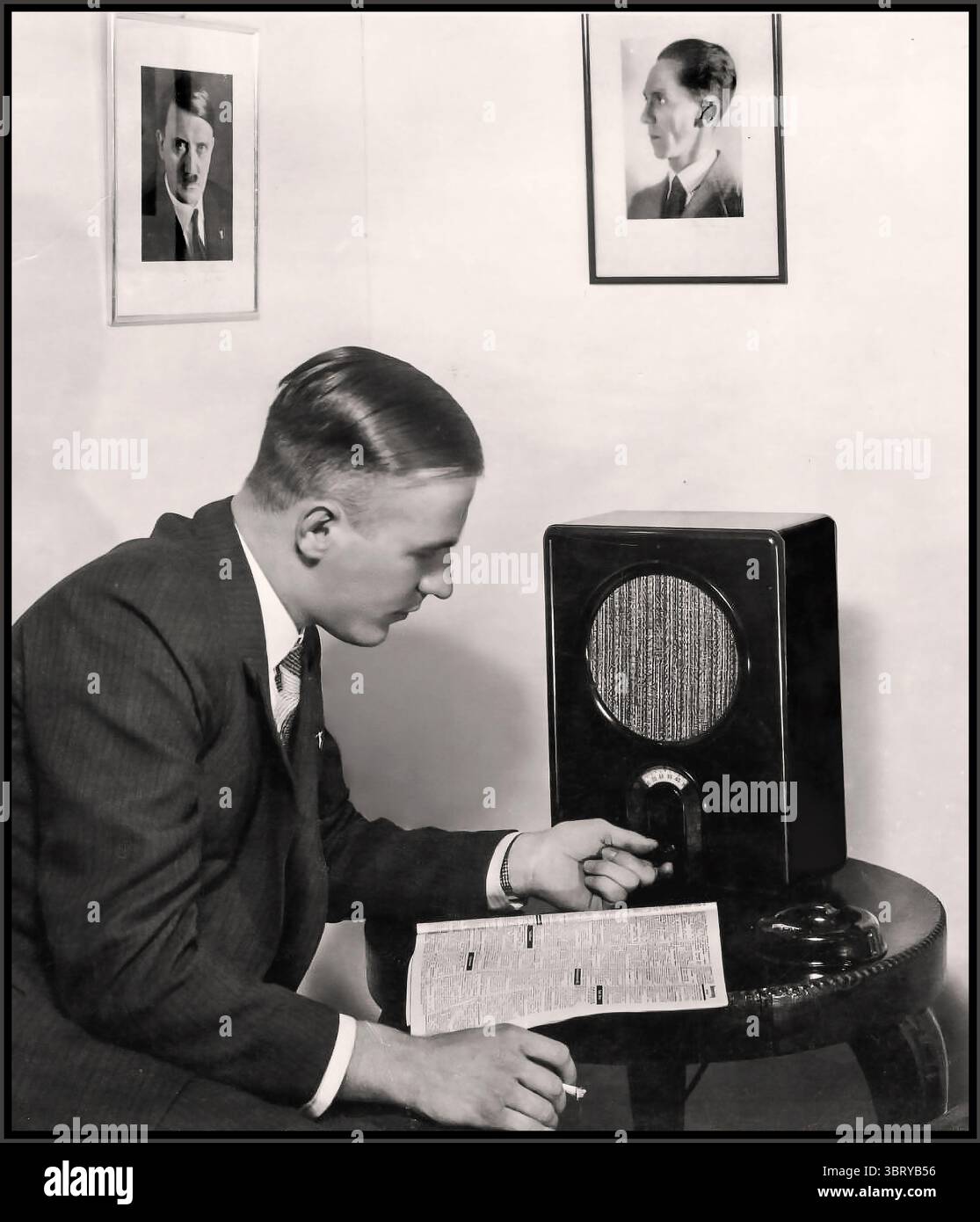 La Germania nazista degli anni '1930 con un ascoltatore di radio maschile che si sintonizza sulle trasmissioni di propaganda nazista con il ricevitore del suo popolo 1933. Ritratti incorniciati di Adolf Hitler e Joseph Goebbels sul muro dietro. Germania nazista 1933 - 1945 Foto Stock