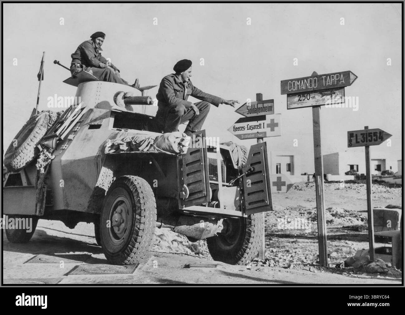 Seconda guerra mondiale in Nord Africa, raffigurante le truppe alleate in un'auto corazzata che tentava di leggere i cartelli stradali tedeschi e italiani nella catturata Derna, Libia. L'auto corazzata sembra essere un modello britannico, probabilmente un Humber o Marmon-Herrington , comunemente usato dalle forze alleate nelle campagne nel deserto. I soldati fanno probabilmente parte di un'unità di ricognizione o pattuglia del Regno Unito, navigando nel territorio catturato sconosciuto indicato dai segnali in lingua straniera. Nord Africa 1943 Foto Stock