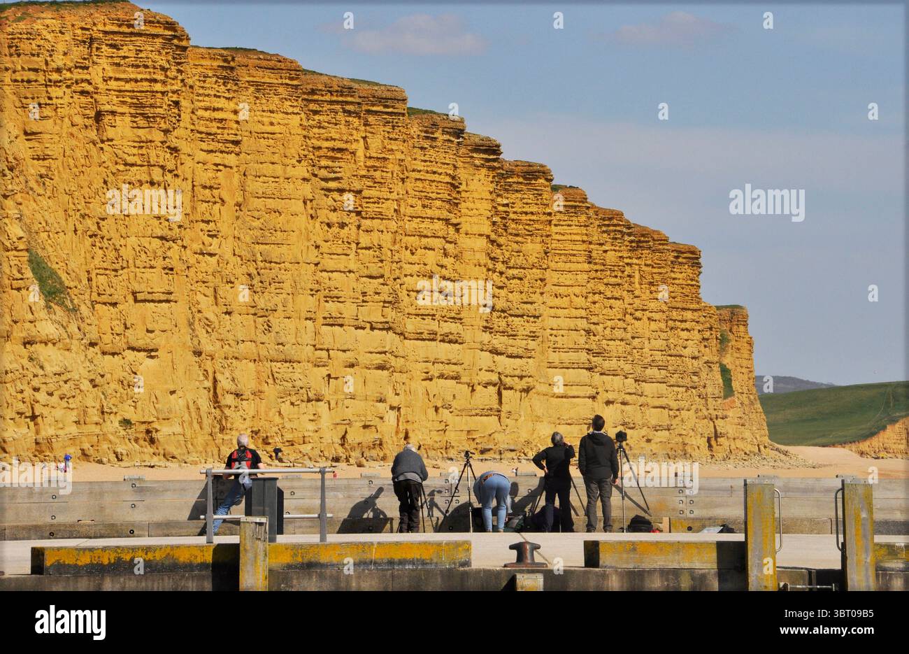I fotografi tentano di catturare la maestosità delle scogliere di arenaria a West Bay nel Dorset dalla fine della frangiflutti. Questo fa parte del suggestivo spettacolo Foto Stock