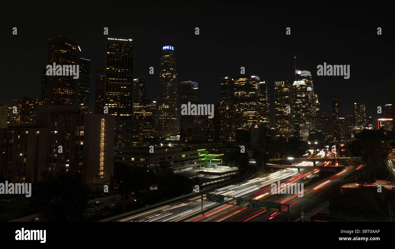 Los Angeles, Stati Uniti - 25 giugno 2025: Veduta aerea di un vivace skyline della città che si illumina di luci dorate, punteggiata dai sentieri sfocati delle auto di passaggio sulle autostrade. Foto Stock