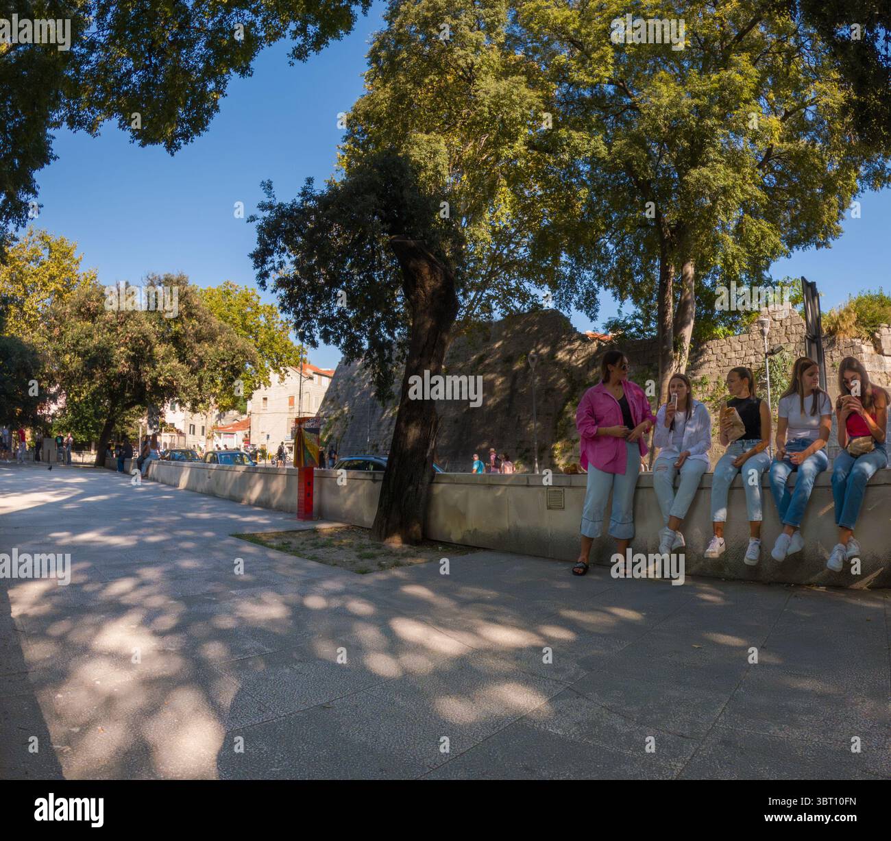 Spalato, Croazia - 8 settembre 2023: Un gruppo di giovani donne si siede su una sporgenza, gustando spuntini e chiacchierando in una giornata di sole a Spalato, Croazia. Foto Stock