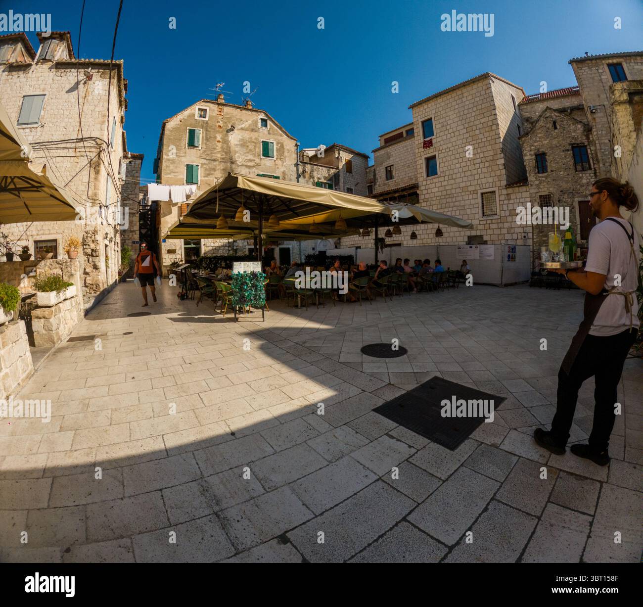 Spalato, Croazia - 8 settembre 2023: Un cameriere porta bevande ai clienti in un caffè all'aperto a Spalato, Croazia. I turisti passeranno a piedi, godendosi le attrazioni e Foto Stock