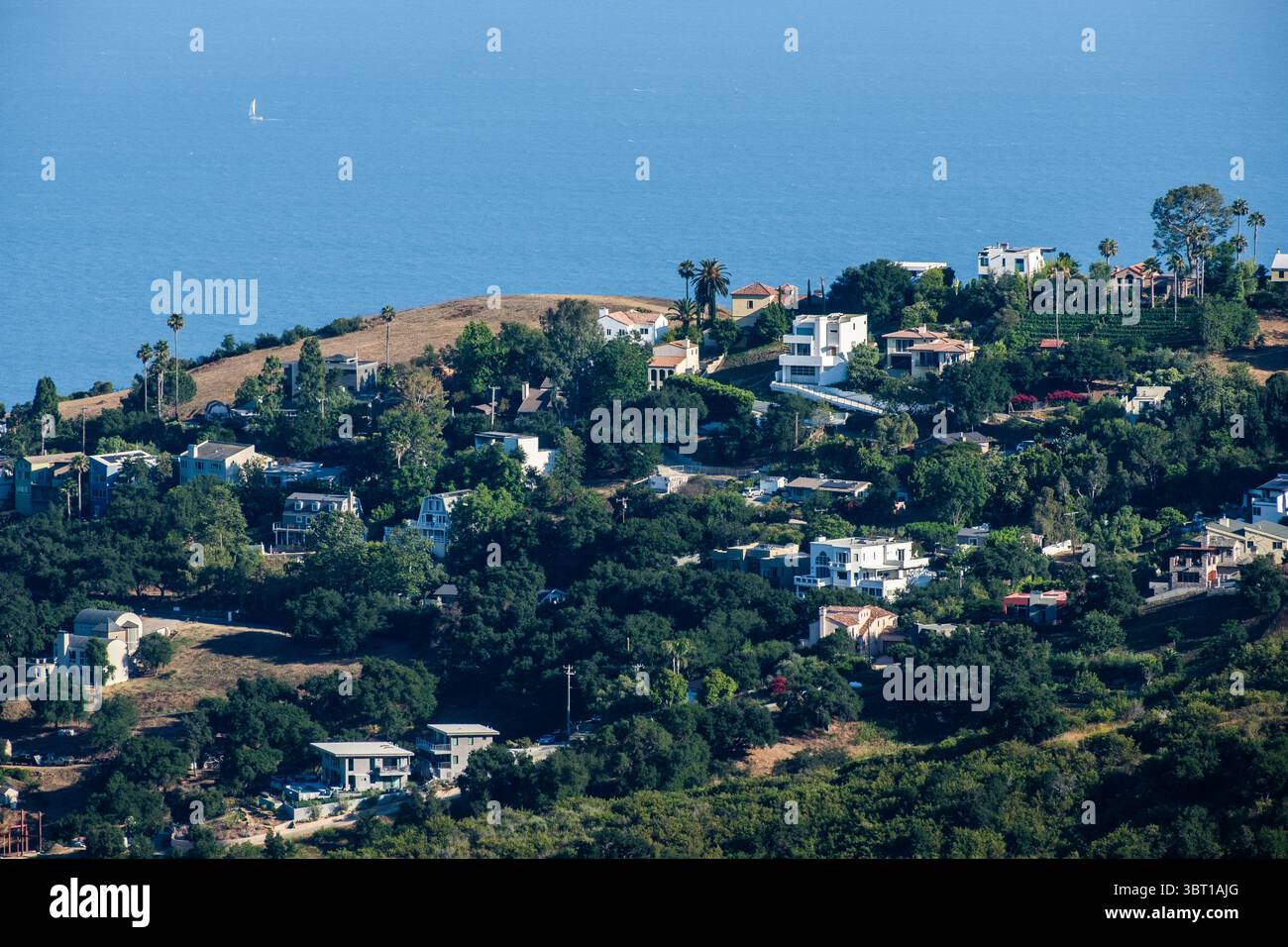Barca a vela sull'Oceano Pacifico e case sulle colline del Corral Canyon a Malibu, California. Foto Stock