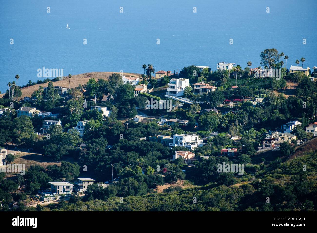 Barca a vela sull'Oceano Pacifico e case sulle colline del Corral Canyon a Malibu, California. Foto Stock