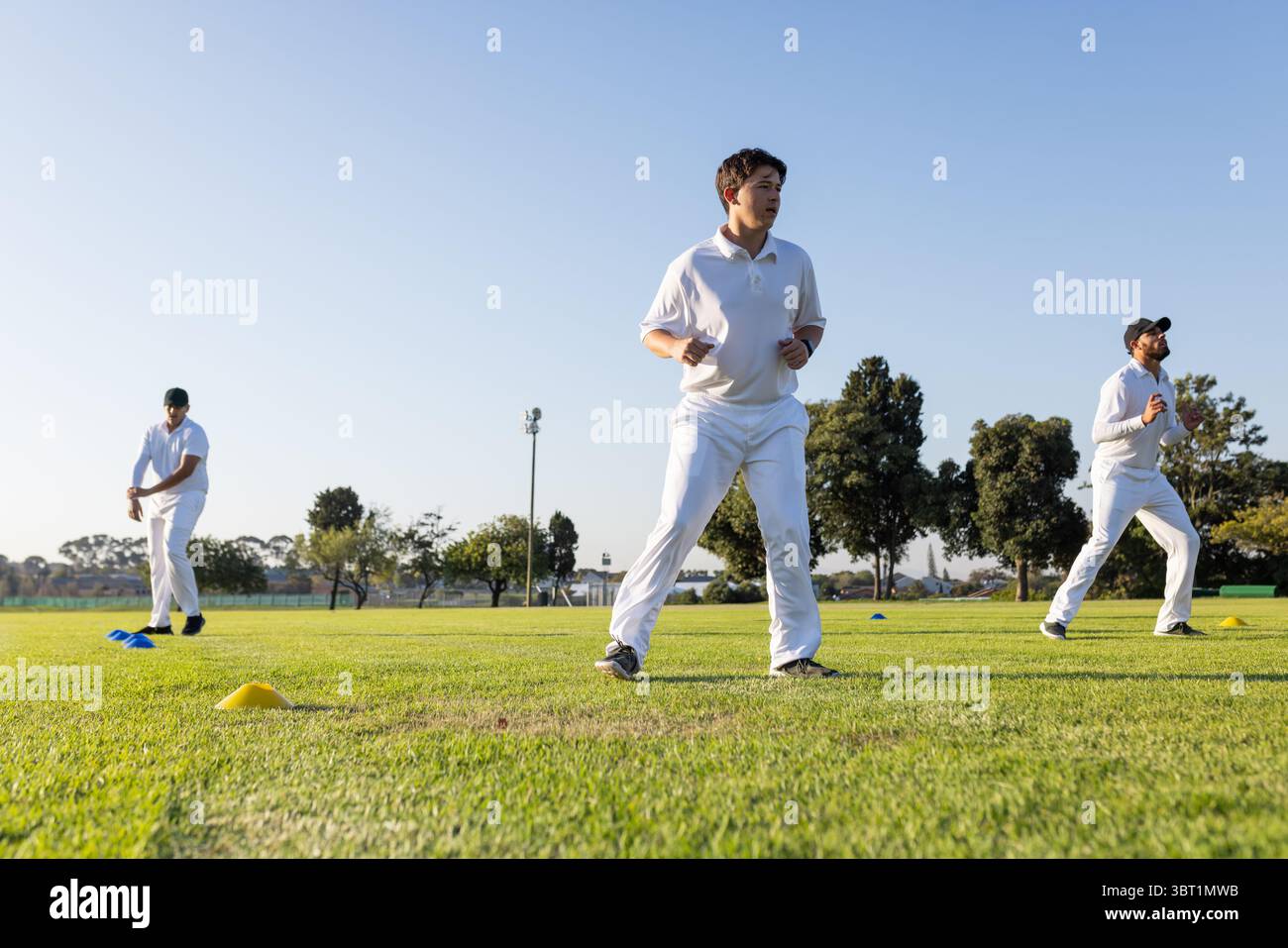 Compagni di squadra maschi di cricket che si riscaldano sul campo di erba tagliata con marcatori a cono gialli Foto Stock