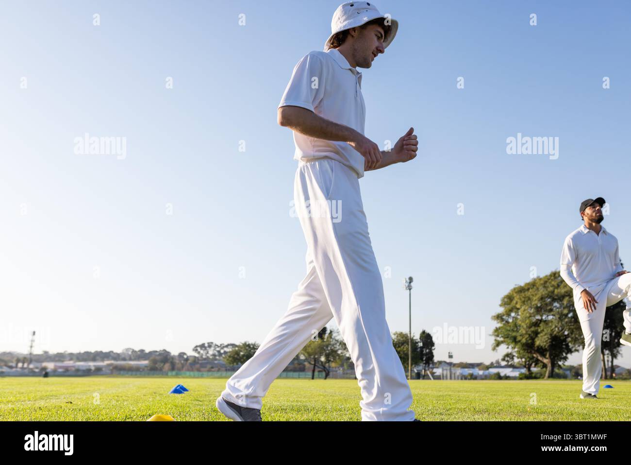 Diversi compagni di squadra maschi che camminano accanto ai coni sul campo di cricket vicino al palo luminoso in bianco, spazio copia Foto Stock