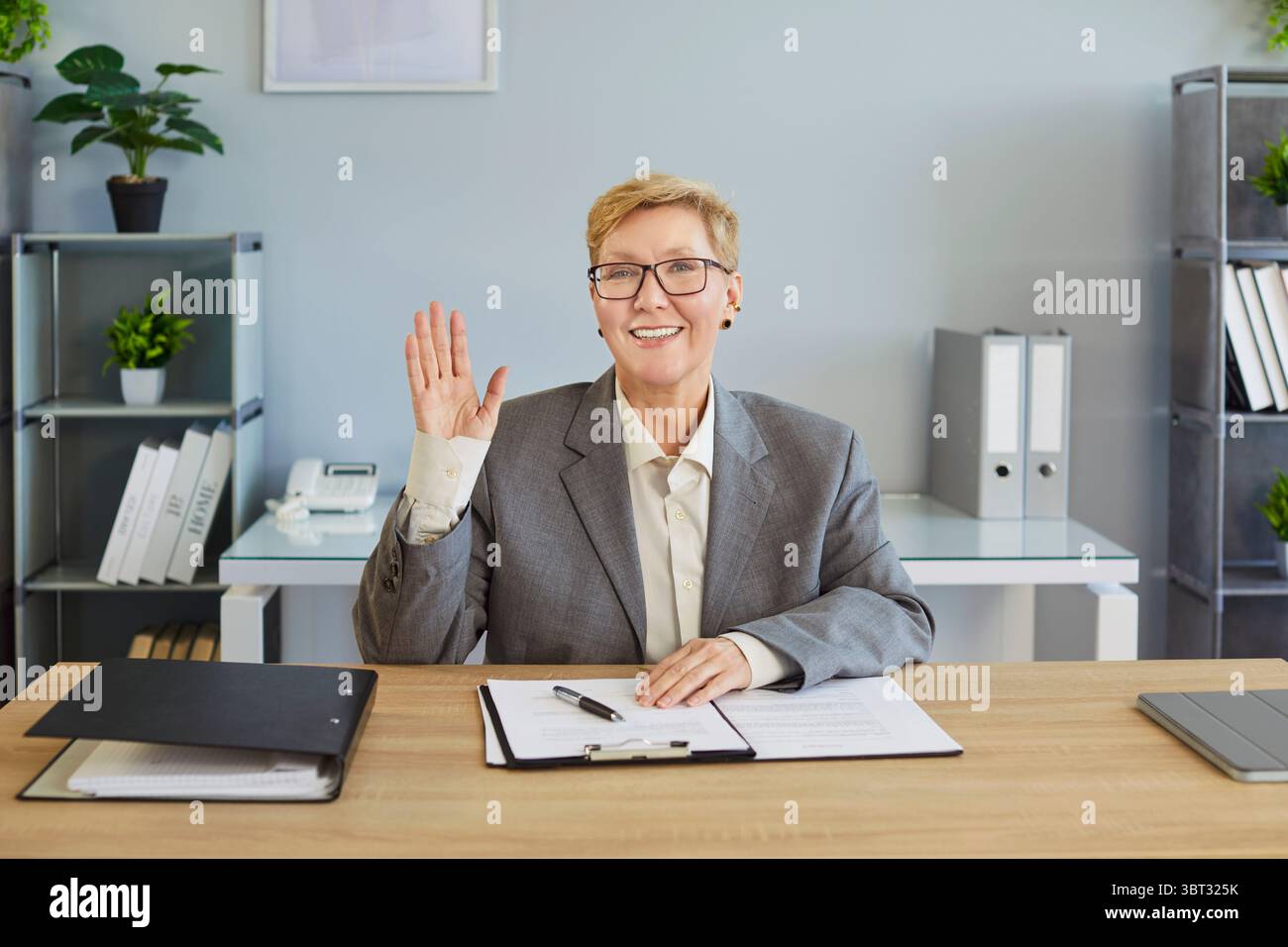 Donna d'affari che saluta in ufficio, interagisce con le videochiamate online con gesti amichevoli Foto Stock