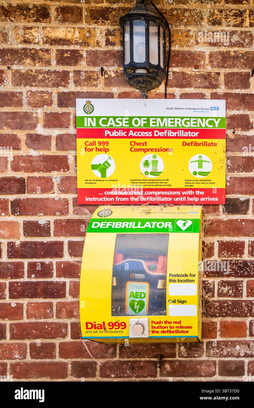 Defibrillatore ad accesso pubblico sul muro in mattoni rustici in un villaggio rurale del Dorset. Foto Stock