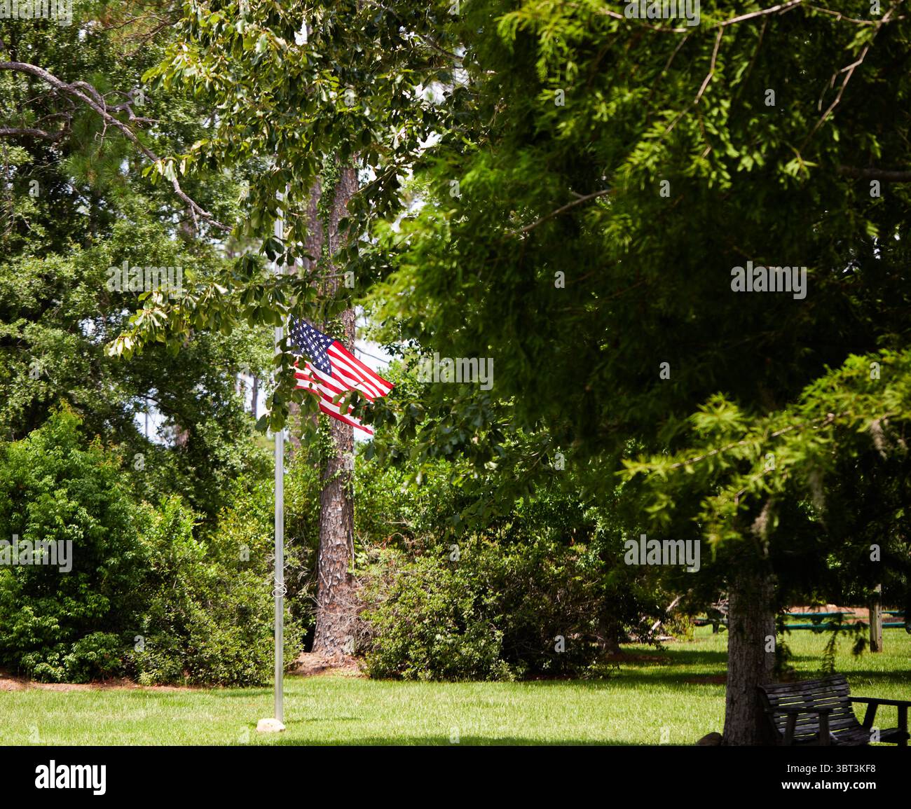 Central Park nella cittadina di Lakeland, Georgia USA, con un ponte ad arco sopra uno stagno, la bandiera degli Stati Uniti e un vecchio trattore internazionale! Foto Stock