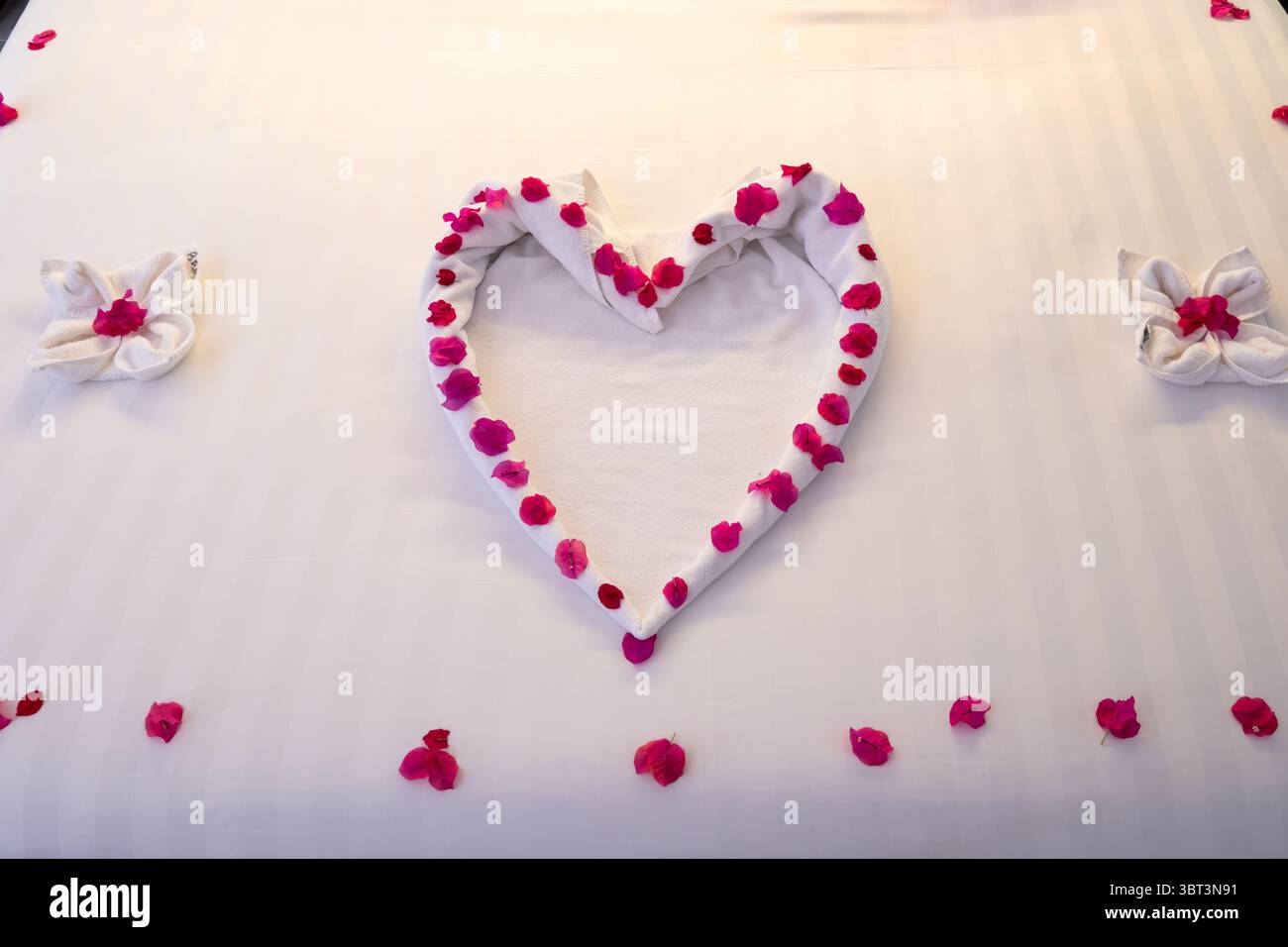 Romantico letto matrimoniale con petali di rosa, asciugamani piegati, cigni e palloncini rossi, arredi per il letto dell'anniversario Foto Stock