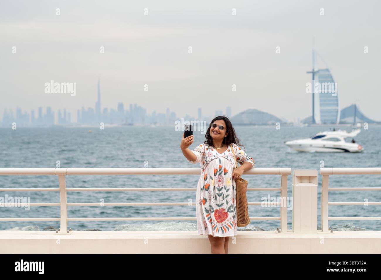 Passeggiata lungo la passeggiata di Dubai con una donna turistica che scatta foto e lo skyline sullo sfondo Foto Stock