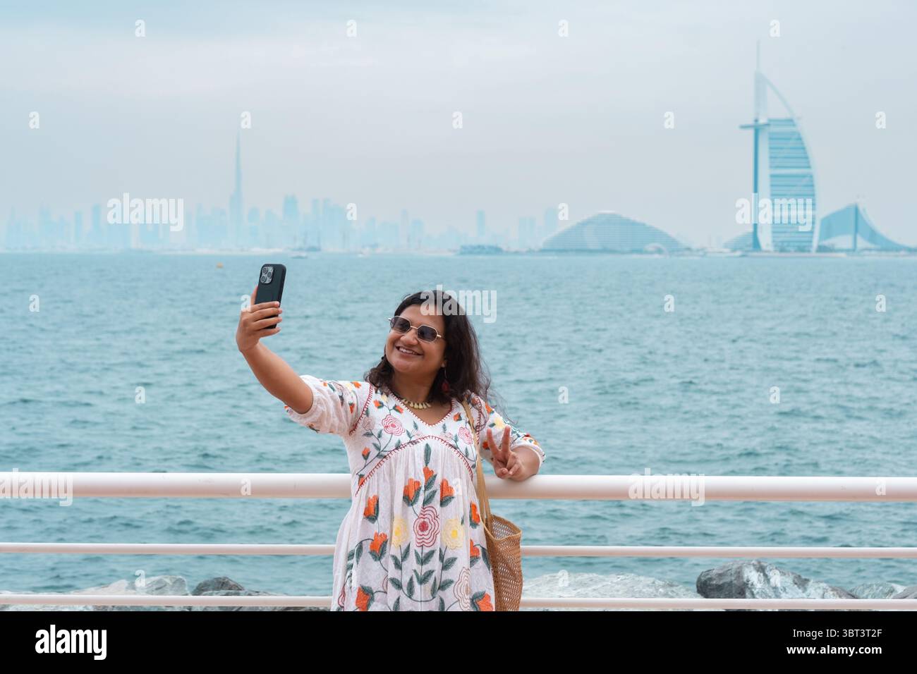 Giovane donna che scatta foto sulla spiaggia di Dubai con Burj al Arab sullo sfondo, donna turistica che esplora dubai Foto Stock