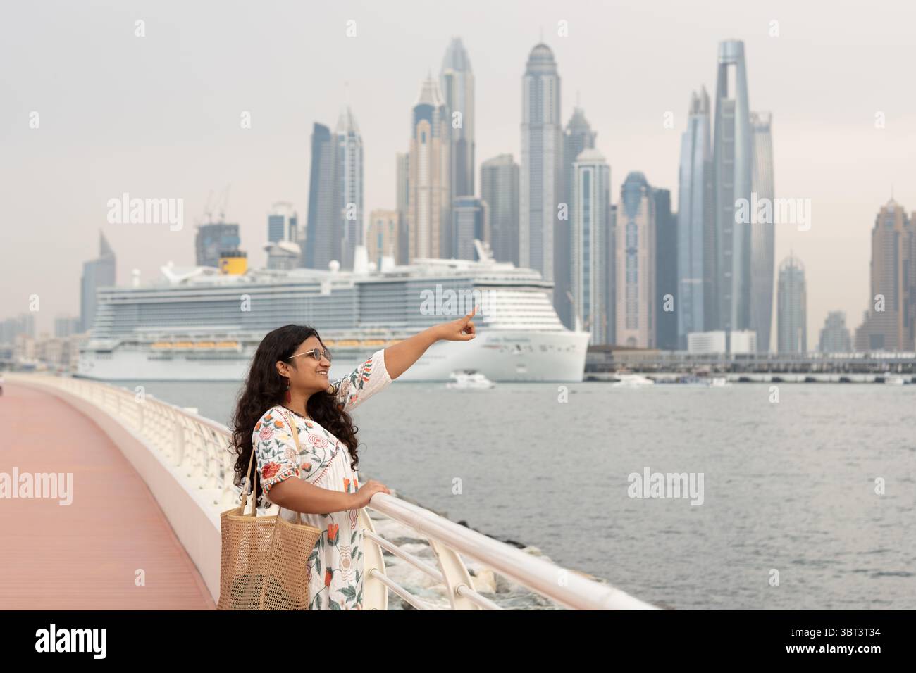 Viaggiatrice donna che esplora Dubai, viaggiatrice da sola che indica uno splendido tramonto a Dubai. Skyline di Dubai Marina con sfondo da crociera Foto Stock