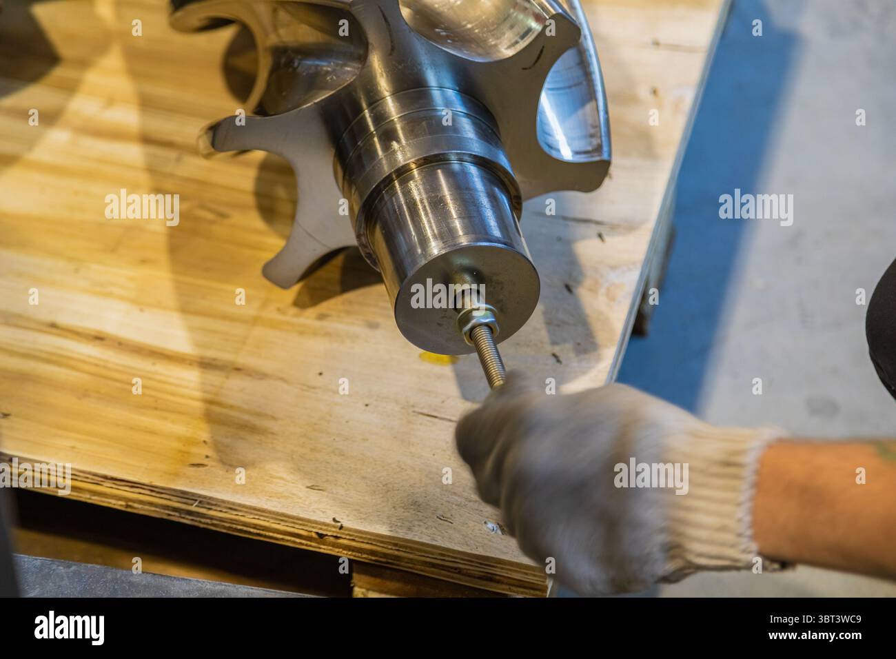 Primo piano di mani con guanti che assemblano una parte meccanica complessa utilizzando un'asta filettata, dimostrando precisione nella produzione industriale Foto Stock
