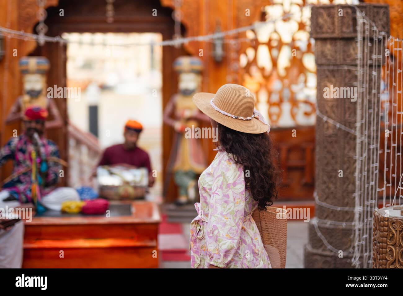 Giovane donna in abito etnico e cappello che esplora il quartiere storico di al Seef a Dubai, circondato dalla tradizionale architettura degli Emirati e dall'atmosfera culturale Foto Stock