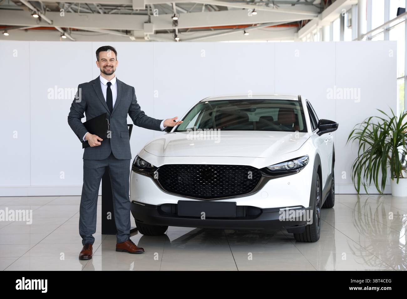 Venditore sorridente con appunti che mostra la nuova auto in salone Foto Stock