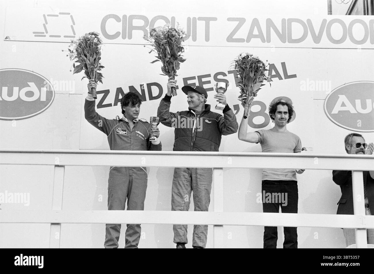 Vincitore delle gare di sabbia Zandvoort Circuit Zandvoort Zandvoort, Whizgle News, Dutch Desk, Paesi Bassi, 1950 - 2000 il 07-08-1983. L'immagine contiene questi argomenti. La scena cattura un momento celebrativo in un evento di corse, probabilmente su un podio. Tre individui si trovano fianco a fianco, ognuno con un trofeo in alto come dimostrazione di vittoria. Le persone sono vestite con l'equipaggiamento da corsa, che include tute colorate e luminose che riflettono le diverse squadre di corse. Questo abbigliamento presenta vari design, con elementi come loghi e patch che evocano un senso di competizione e spirito di squadra. La figura centrale Foto Stock