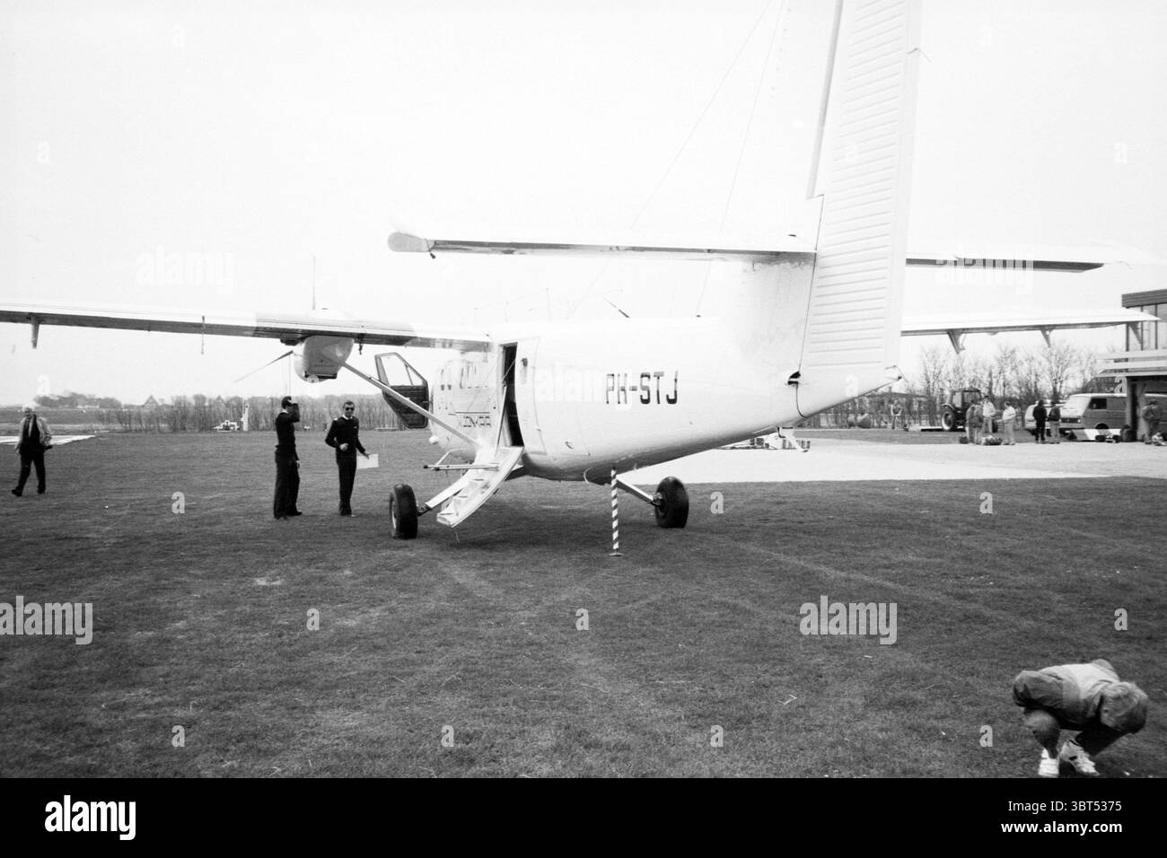Aeroplano Texel Airport Flying, Whizgle News, Dutch Desk, Paesi Bassi, 1950 - 2000 il 21-04-1987. Questi sono gli argomenti nell'immagine. La scena presenta un piccolo aereo leggero parcheggiato su un'area erbosa. L'aereo è prevalentemente bianco, con una sottile lucentezza che riflette il cielo sovrastante. Ha un design ad ala bassa, con caratteristiche distintive tra cui una coda che si solleva bruscamente sul retro. Le ruote dell'aeromobile sono posizionate su un contrassegno di terra a strisce, che indica che è a terra e che è possibile che sia in attesa di manutenzione o ispezione. In primo piano, due persone sono impegnate in attività vicino all'intelligenza artificiale Foto Stock