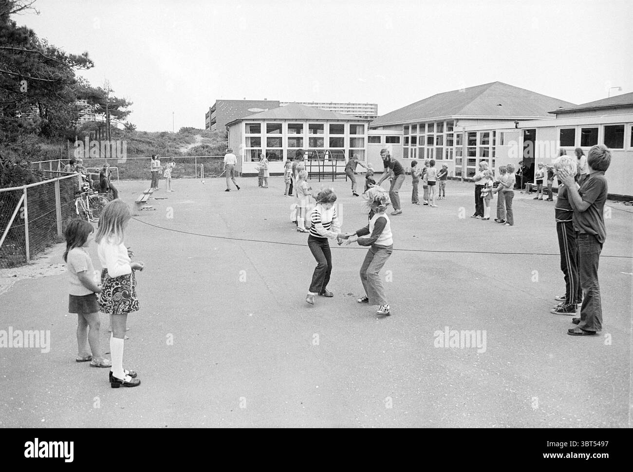 Danza popolare per bambini ballo popolare, Whizgle News, Dutch Desk, Paesi Bassi, 1950 - 2000 il 06-08-1973. Questi argomenti sono mostrati nell'immagine. La scena raffigura un vivace parco giochi pieno di bambini impegnati in varie attività. In primo piano, due bambini saltano entusiasticamente la corda; la ragazza a sinistra ha un sorriso giocoso, mentre il ragazzo a destra è concentrato e determinato. Entrambi sono vestiti con un abbigliamento casual, con la ragazza con una maglia a righe e il ragazzo con una camicia leggera e pantaloncini corti. Nelle vicinanze, un gruppo di bambini si trova in varie posture. Alcuni stanno aspettando il loro turno, mentre o Foto Stock