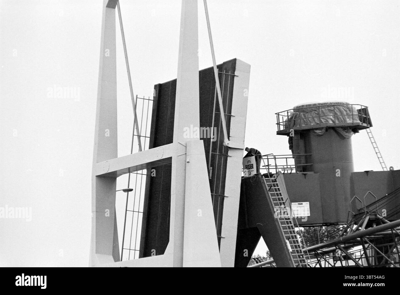 Transport Figee Rotterdam Rotterdam Rotterdam, Whizgle News, Dutch Desk, Paesi Bassi, 1950 - 2000 on 27-08-1992. Questi sono gli elementi dell'immagine. La scena presenta una struttura industriale con un'attenzione particolare a un grande componente simile a un ponte, caratterizzato dai suoi alti supporti angolari bianchi che si innalzano verso l'alto, suggerendo resistenza e stabilità. Il ponte sembra essere in posizione elevata, con una superficie visibilmente scura e piatta che si estende orizzontalmente tra i supporti, suggerendo il suo scopo funzionale. Da un lato, c'è un'enorme unità di macchinari, dipinta in un rosso profondo e audace, che co Foto Stock