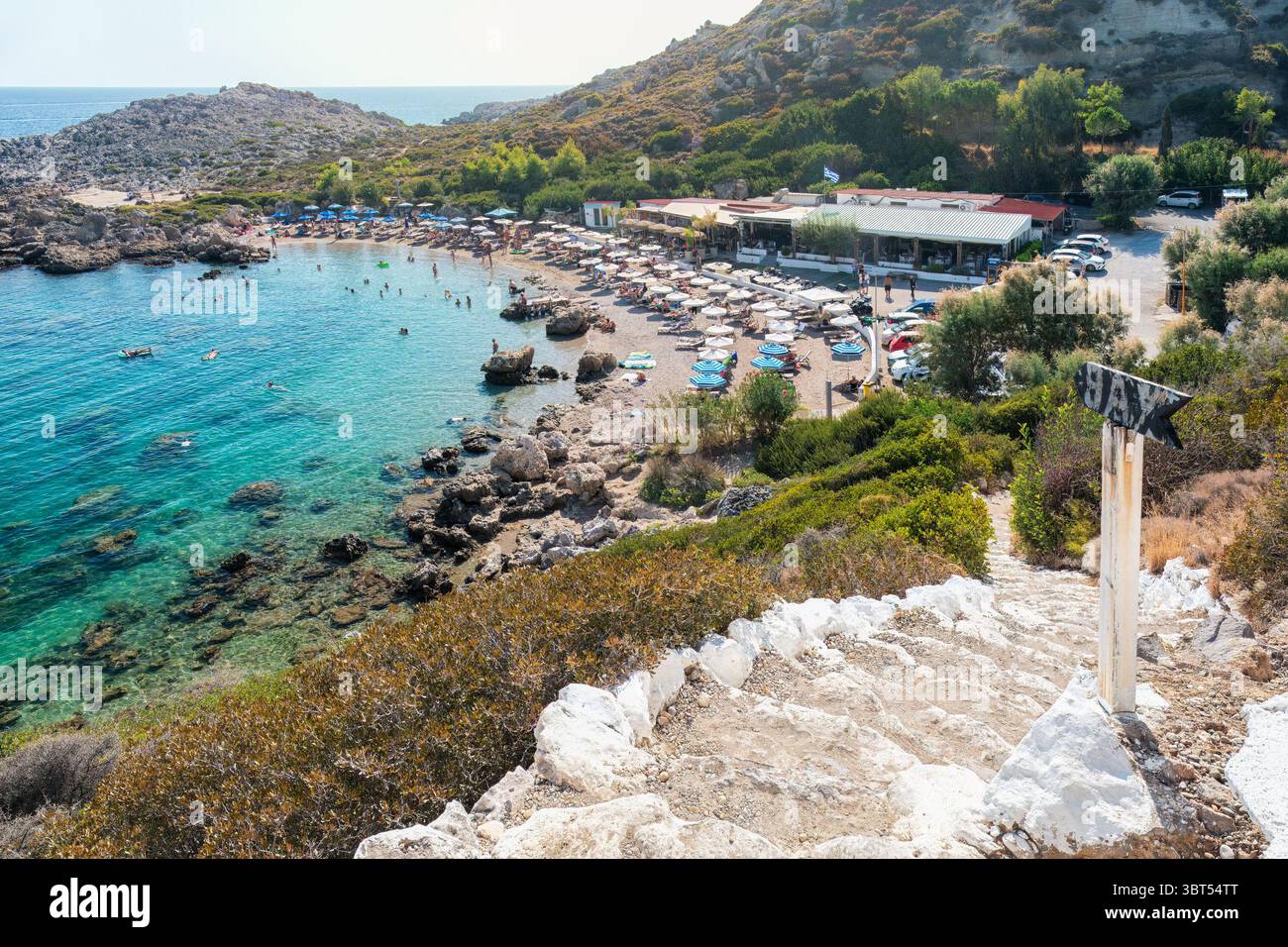 La scena costiera presenta acque turchesi cristalline, spiagge rocciose, bagni e ombrelloni colorati, invitanti momenti di relax e divertimento in un ambiente all'aperto sereno Foto Stock