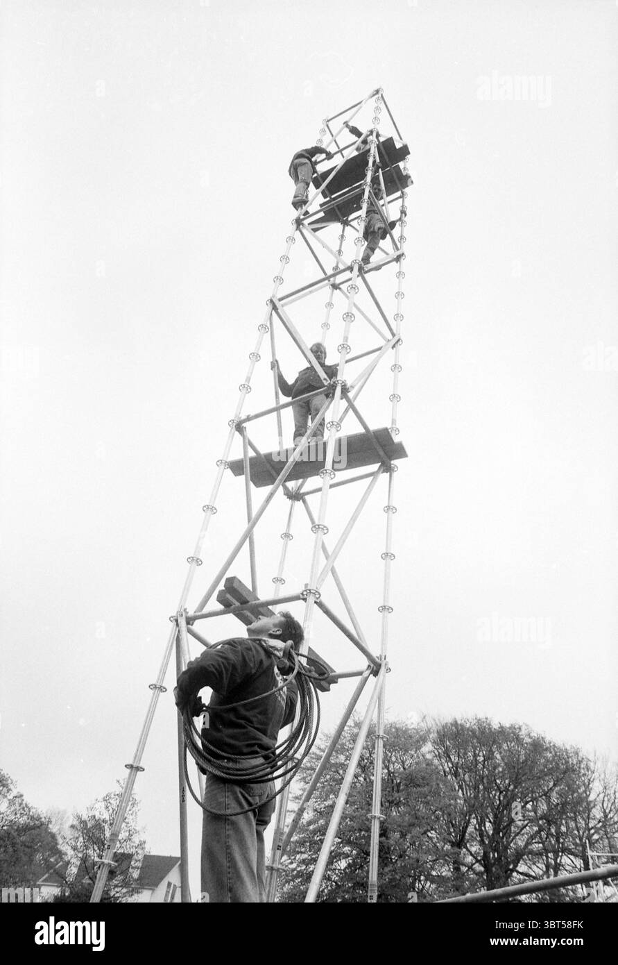 Fase di costruzione della bambola di liberazione, Whizgle News, Dutch Desk, Paesi Bassi, 1950 - 2000 il 30-04-1991. Questi sono gli elementi dell'immagine. La scena cattura un gruppo di persone impegnate in un compito complicato in cima a un'alta struttura metallica che assomiglia a una torre. La struttura della torre è costituita da travi interconnesse, che presentano un design industriale con una serie di piattaforme e attrezzature a varie altezze. Tre persone sono posizionate a diversi livelli. L'individuo più alto sta lavorando in modo metodico, magari regolando o fissando le attrezzature, mentre un'altra persona è posizionata su un p inferiore Foto Stock