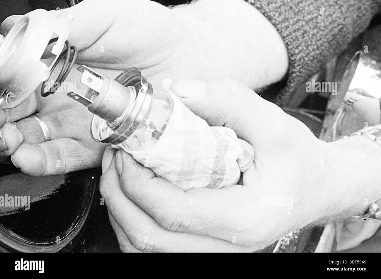 V.W. ricambi auto per libretto di istruzioni Motors moto race, Whizgle News, Dutch Desk, Paesi Bassi, 1950 - 2000 il 23-11-1963. L'immagine mostra questi argomenti. Nella scena, sono presenti due mani, tenendo in mano un piccolo oggetto metallico delicatamente avvolto in un panno, suggerendo cura e attenzione. Le mani appaiono intemprate, a indicare l'esperienza e forse un grado di età, con una texture visibile e un pizzico di grana, enfatizzato dai toni monocromatici. L'oggetto metallico ha una superficie liscia e lucida che riflette la luce in un modo che suggerisce che è realizzato in cromo o acciaio inossidabile. Possiede Foto Stock