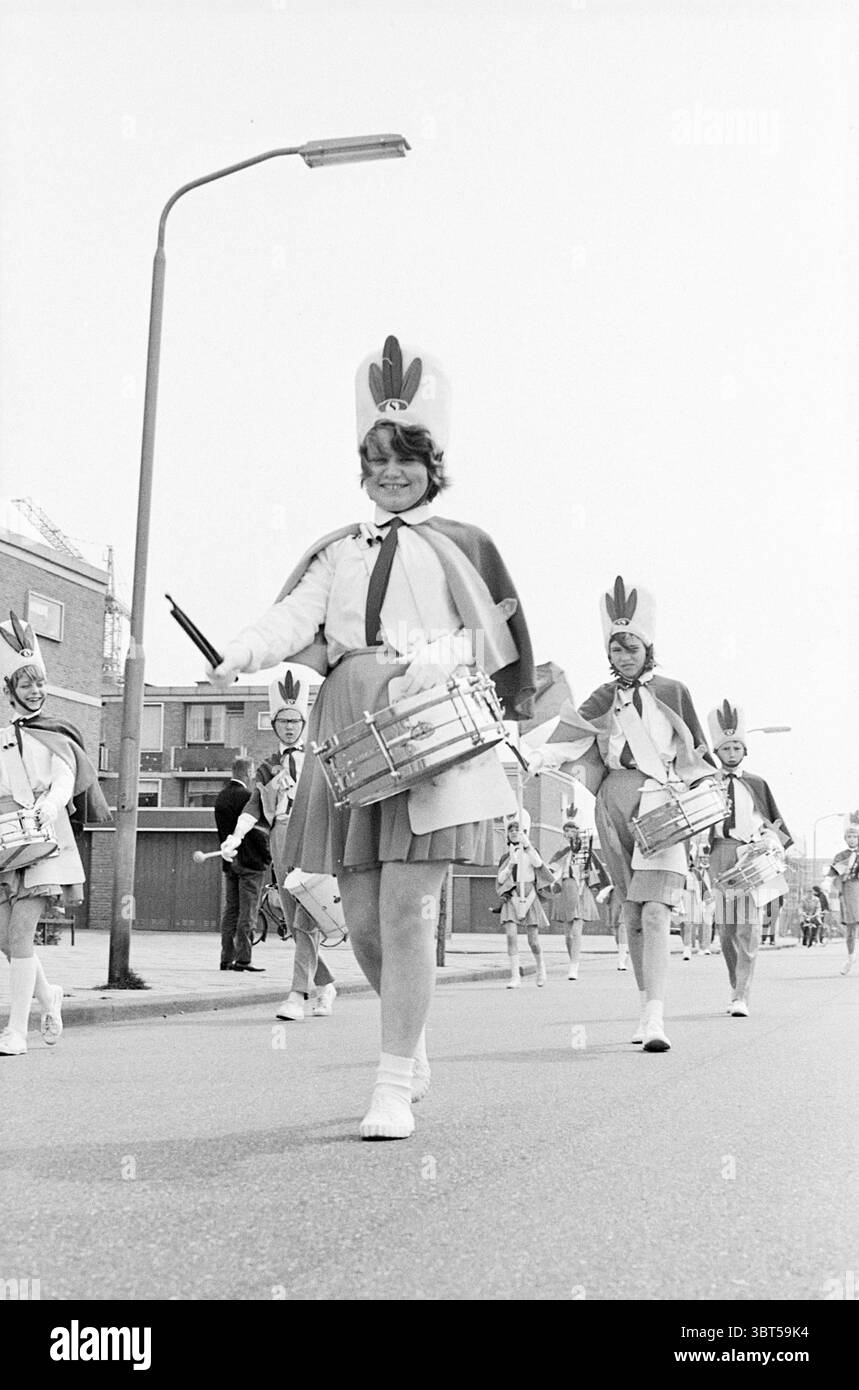 Drum band show Schalkwijk Festival festeggiamenti e manifestazioni Haarlem Frankrijklaan Paesi Bassi, Whizgle News, Dutch Desk, Paesi Bassi, 1950 - 2000 il 04-05-1967. Questi argomenti vengono visualizzati nell'immagine. La scena cattura una vivace parata con un gruppo di giovani individui che marciano lungo una strada. Sono adornate con uniformi luminose, caratterizzate prevalentemente da colori bianco e pastello, completate da un caratteristico copricapo che sfoggia un audace design simile a una piuma. Ogni membro ha un tamburo a rullante, alcuni decorati con finiture metalliche lucide che catturano la luce. L'impostazione sembra essere un urb Foto Stock