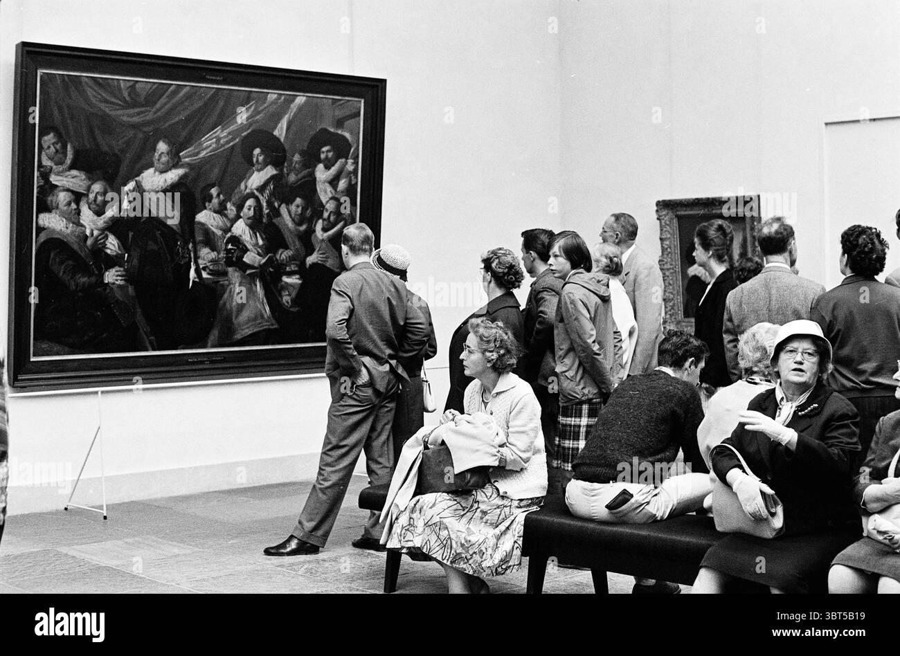 Gestione della mostra Frans Hals Museo Frans Hals Museo Frans Hals, Whizgle News, Dutch Desk, Paesi Bassi, 1950 - 2000 il 23-07-1962. L'immagine contiene questi argomenti. In una spaziosa galleria adornata da alti soffitti e pareti bianche, un grande e suggestivo dipinto domina la scena. L'opera d'arte, con figure vestite in abiti storici, cattura l'attenzione degli spettatori con i suoi colori ricchi e la sua composizione dinamica. Le figure del pezzo trasudano un senso di autorità e presenza, le loro espressioni variano da contemplativa a coinvolgente. Un gruppo diversificato di visitatori si riunisce in questo centro Foto Stock