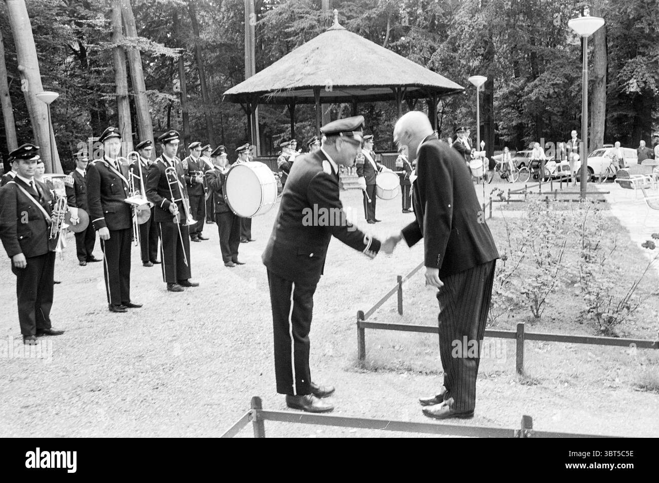 Reception Mr. De Ronde Noord Zuid Hollandse Vervoersmaatschappij N.V. NZ, Whizgle News, Dutch Desk, Paesi Bassi, 1950 - 2000 il 06-09-1969. Questi argomenti vengono visualizzati nell'immagine. In un ambiente tranquillo all'aperto, due uomini sono impegnati in una stretta di mano in prima linea. Uno degli uomini è vestito con un'uniforme formale, con una giacca scura ornata da distintivi, che suggerisce una posizione di autorità o rispetto. L'altro uomo è in tuta formale, presentando un'aria di eleganza e civiltà. Le loro espressioni trasmettono rispetto reciproco e cameratismo. Intorno a loro, un piccolo gruppo di individui in uniforme si erge Foto Stock