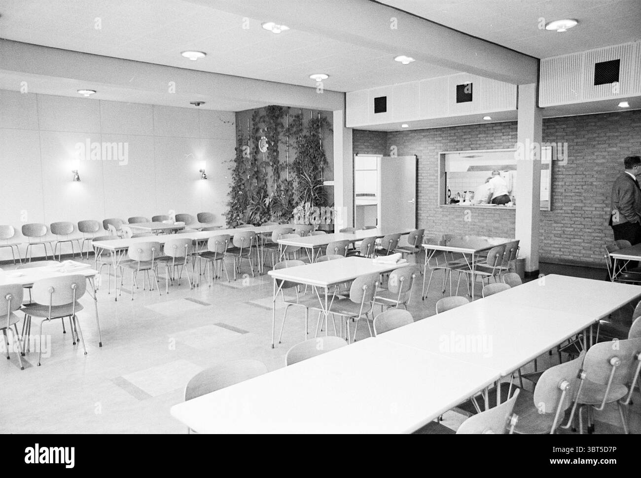 Relazione "De Typhoon" in Zaandam Haarlems Dagblad ecc. e IJmuider Courant e Koeri relazione, Whizgle News, Dutch Desk, Paesi Bassi, 1950 - 2000 il 17-10-1968. Questi sono gli argomenti nell'immagine. La scena si snoda in una spaziosa caffetteria, caratterizzata da un design moderno della metà del secolo. Le pareti sono caratterizzate da una palette neutra di grigi tenui, mentre una parete d'accento testurizzata in mattoni aggiunge calore e profondità. L'illuminazione emana dai soffitti circolari, diffondendo una luce soffusa in tutta la stanza. Diverse file di lunghi tavoli rettangolari si estendono sul pavimento, con superfici che brillano sotto il labbro Foto Stock