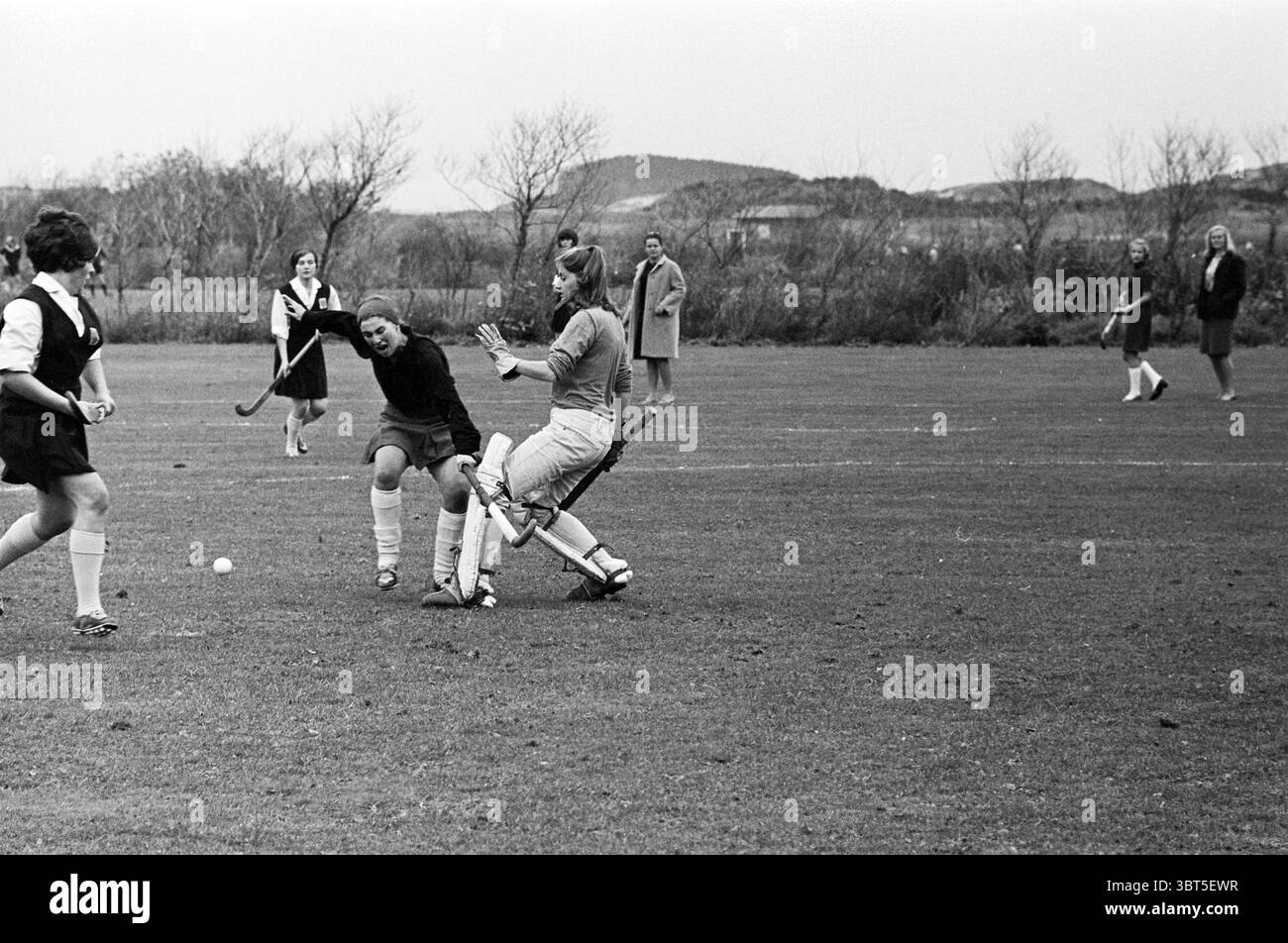 Hockey Match Ladies., Whizgle News, Dutch Desk, Paesi Bassi, 1950 - 2000. Questi argomenti vengono visualizzati nell'immagine. La scena cattura un momento vivace su un campo erboso, dove si sta svolgendo una partita di hockey. Un gruppo di atleti è impegnato nello sport, i loro movimenti dinamici ed energici. In primo piano, due giocatori sono in uno scontro attivo: Un giocatore, vestito con abiti scuri, sembra manovrare la palla con abilità, mentre l'altro, indossando un equipaggiamento protettivo di colore chiaro, sta tentando di intercettare il gioco. Entrambi sono concentrati e determinati, mostrando il loro atletismo. Foto Stock