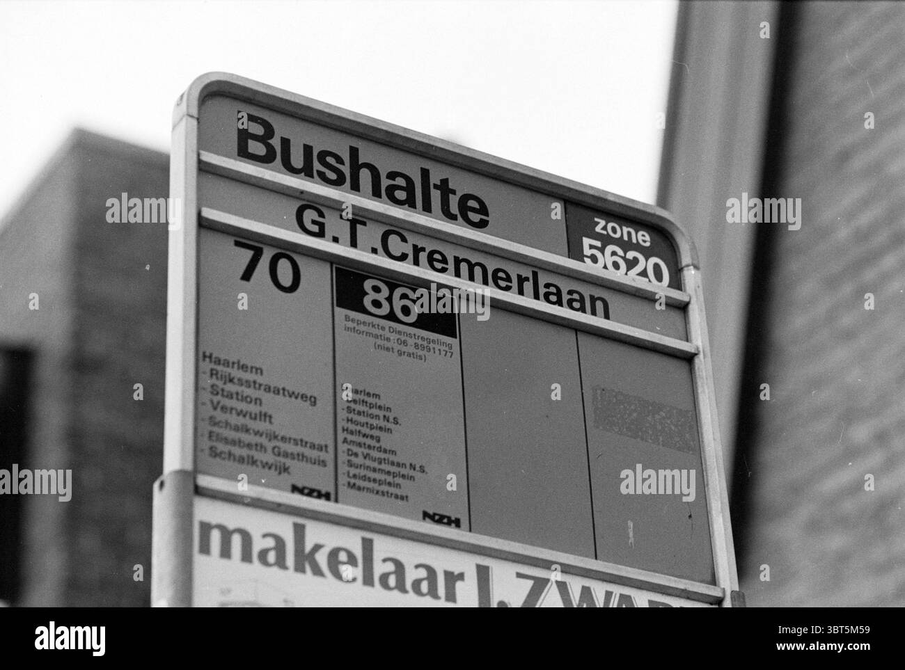 Fermata dell'autobus 'G.T. Cremerlaan' S'poort Santpoort-Noord J.T. Cremerlaan, Whizgle News, Dutch Desk, Paesi Bassi, 1950 - 2000 al 27-12-1990. L'immagine include questi argomenti. La scena presenta un segnale di fermata dell'autobus ben visibile sullo sfondo dell'architettura urbana. Il cartello si erge alto, con una struttura metallica che ha un aspetto intempestivo, a indicare anni di servizio. La parte superiore del cartello ha un design strutturato che presenta le informazioni in modo chiaro e organizzato. Comprende le linee di autobus chiaramente numerate, che indicano i servizi disponibili (70 e 86). Sotto il numero del percorso Foto Stock