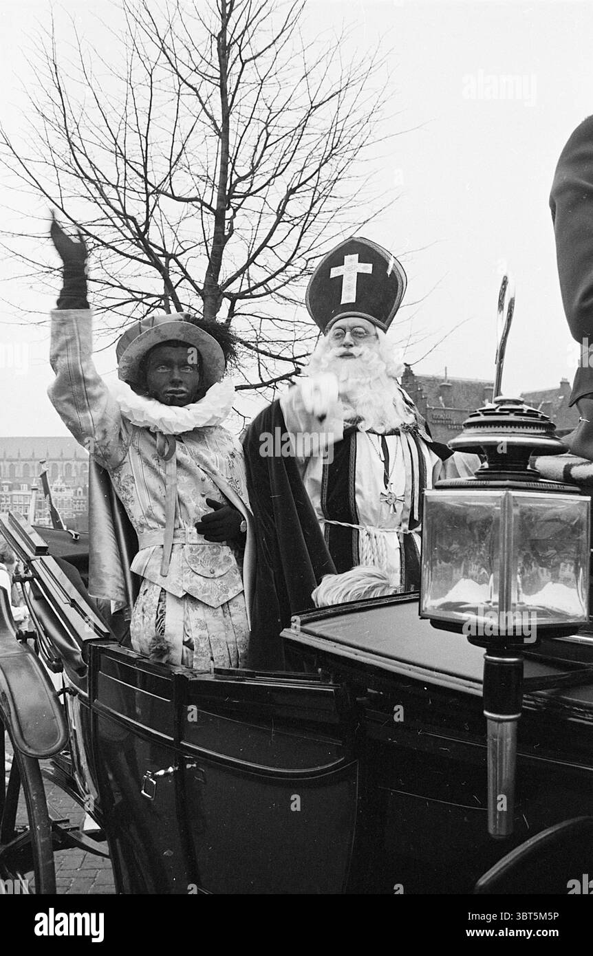 Arrivo di San Nicola a Haarlem St. Nicholas Sinterklaas, Whizgle News, Dutch Desk, Paesi Bassi, 1950 - 2000 il 17-11-1965. L'immagine mostra questi argomenti. La scena presenta due figure nelle immediate vicinanze all'interno di un'impostazione carrello. Una figura, vestita con abiti decorati di colore chiaro, presenta un colletto bianco con volant. Il tono della sua pelle è più scuro, fornendo un contrasto sorprendente con i suoi vestiti. Solleva un braccio, magari con un gesto di saluto o di entusiasmo, che aggiunge un elemento vivace alla scena. Accanto a lui, la seconda figura è rivestita di grandi paramenti caratteristici di una tradizione Foto Stock